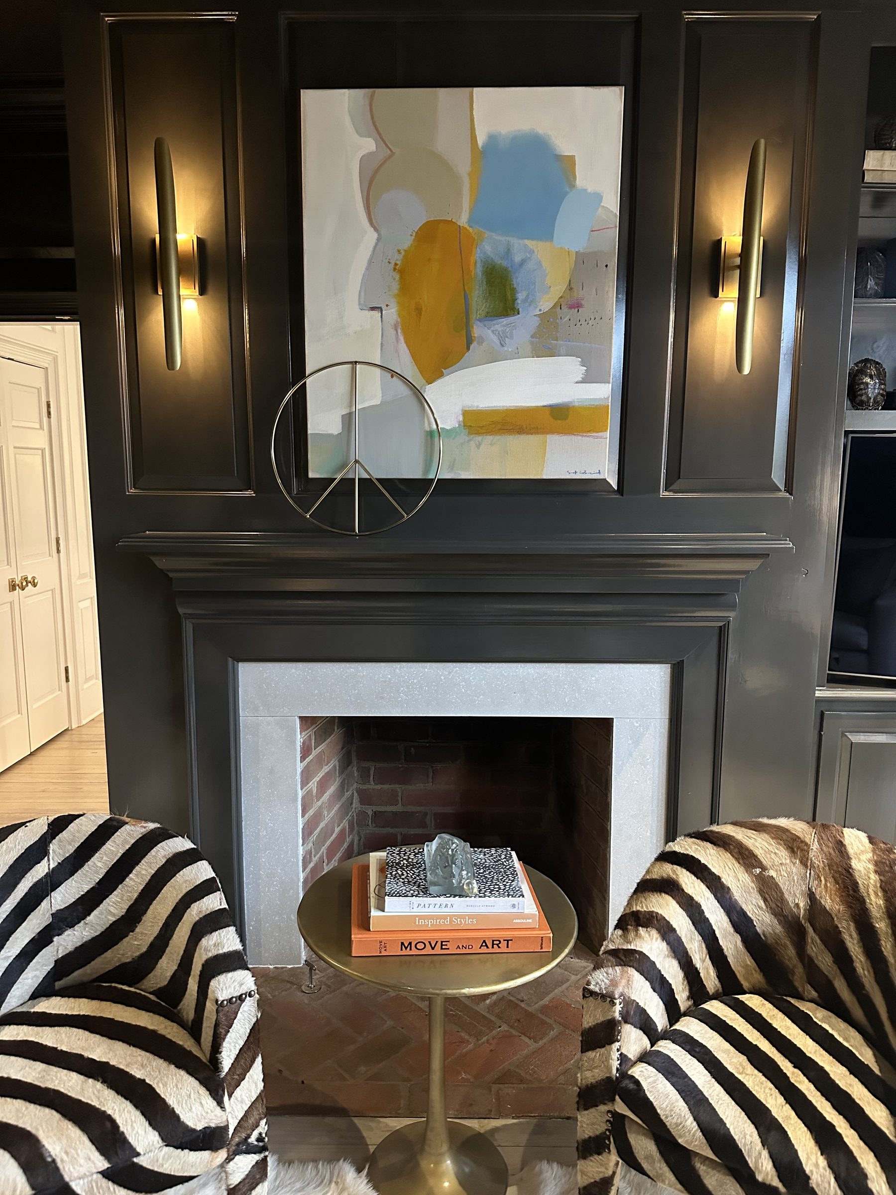 Charcoal paneled fireplace wall with brass sconces and zebra swivel chairs