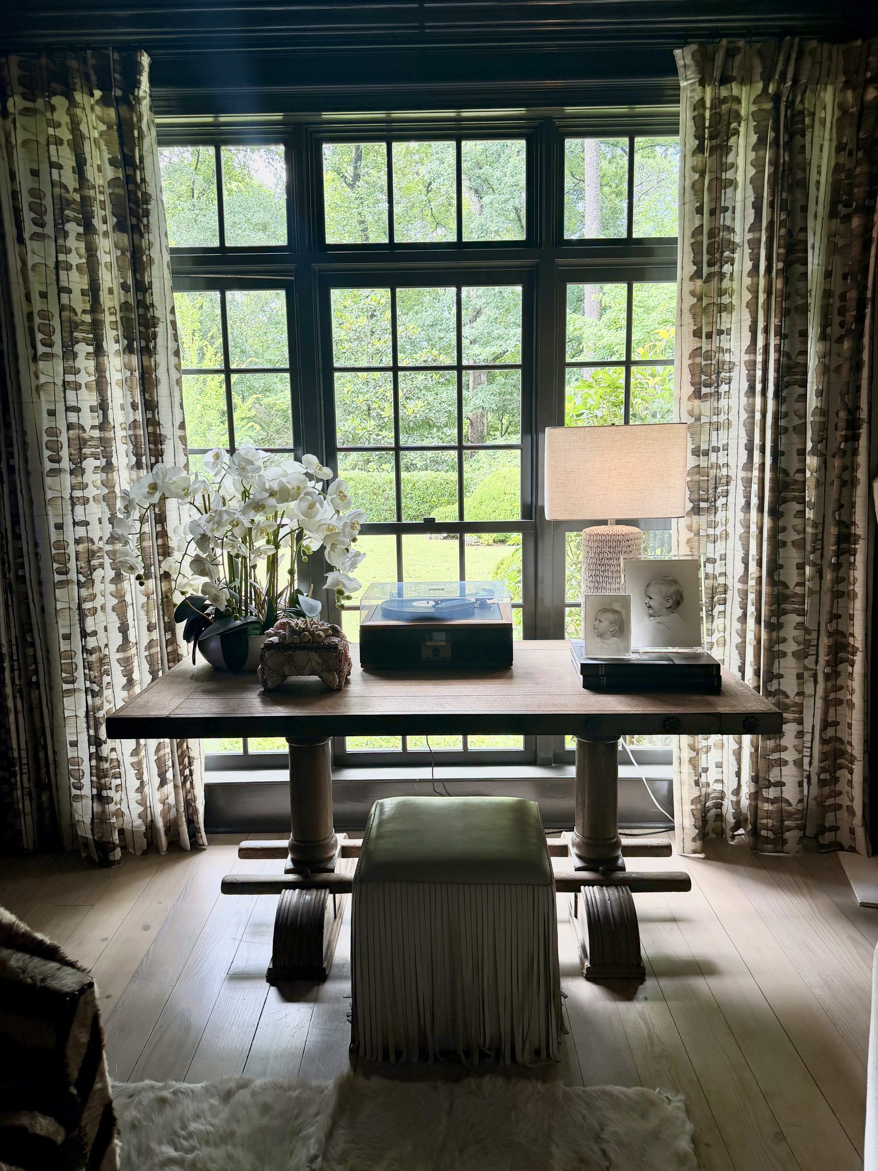 Study with dark trimmed windows, antique trestle table, record player and fringed leather stool